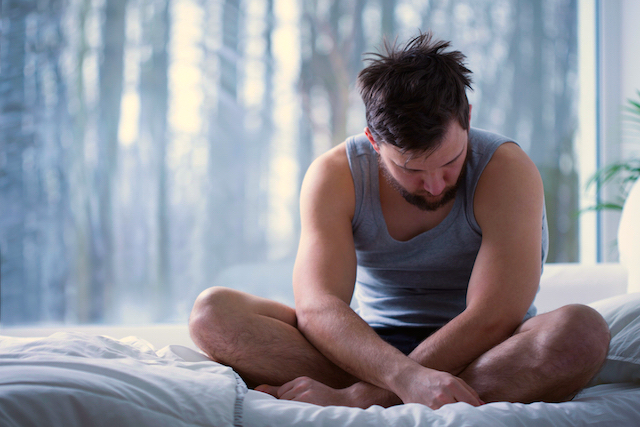 Depressed insomniac man sitting on bed in daylight